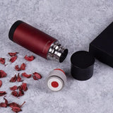 Thermos rouge mat gravé au nom, ouvert sur son col en acier inoxydable, à côté de son bouchon et de son capuchon noir