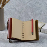 Carnet vintage marron à anneaux, pages kraft, ouvert avec le stylo rouge glissé à l'intérieur